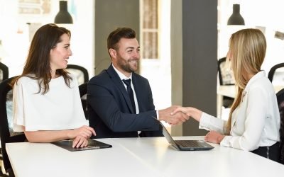 Smiling young couple shaking hands with an insurance agent or investment adviser. Three people meeting in an office reaching an agreement